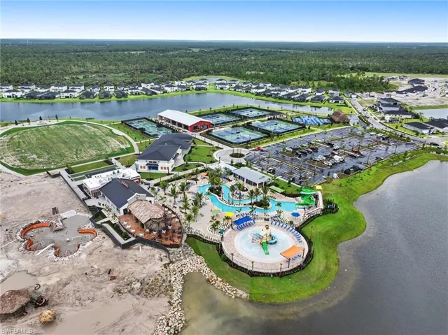 Aerial perspective of community recreational facilities featuring a multi-pool aquatic center, tennis courts, grass sports field, and paved parking area