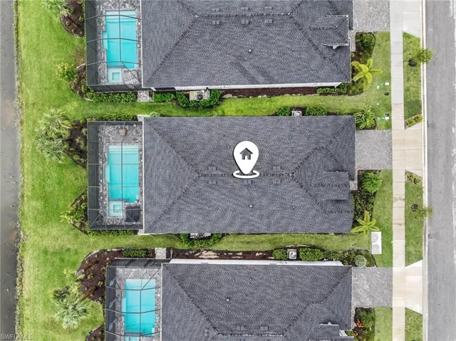 Aerial view featuring a screened-in swimming pool, paved pool deck, manicured lawn, and asphalt shingle roofing