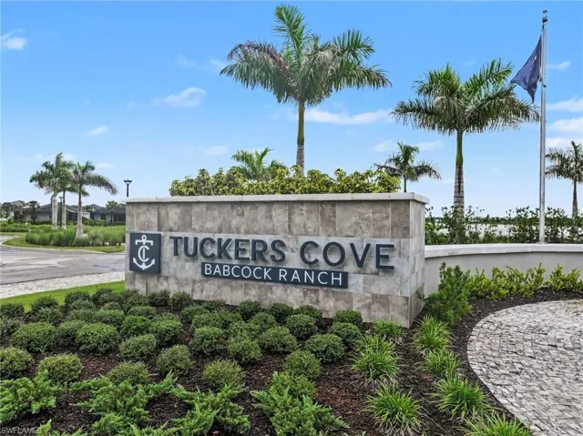 Stone-clad entrance monument featuring dimensional lettering, manicured landscaping, palm trees, and decorative stone paver accents