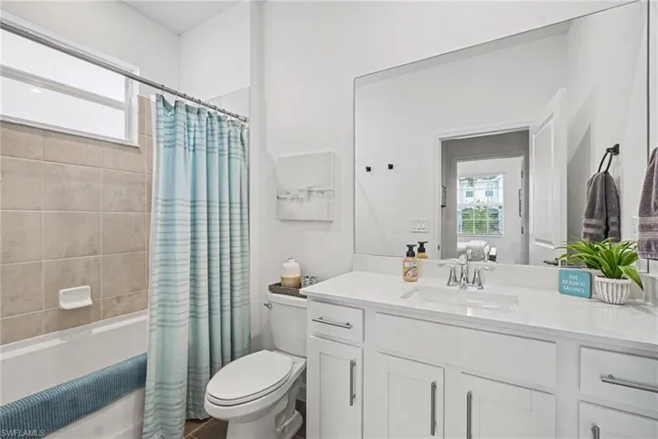 Bathroom featuring white cabinetry, solid-surface countertop with an integrated rectangular sink, wall-spanning mirror, and a tub-shower combination with neutral-toned wall tile