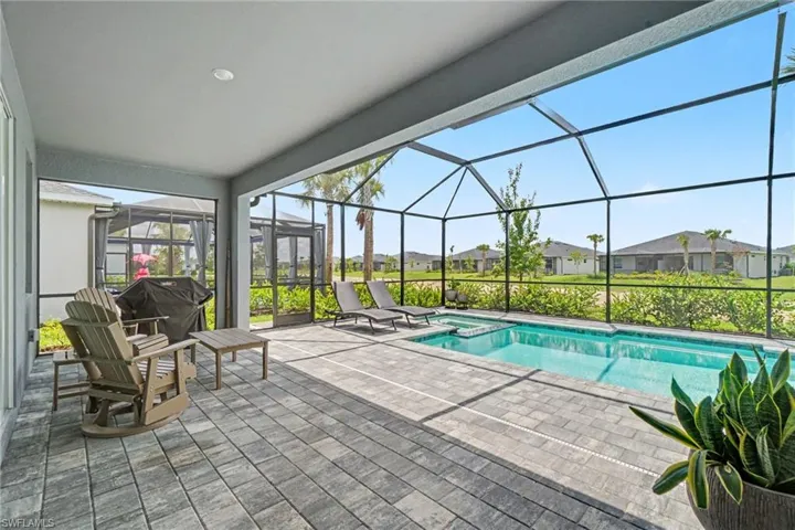 Covered patio with paver flooring, screen-enclosed pool, built-in spa, and concrete block perimeter wall