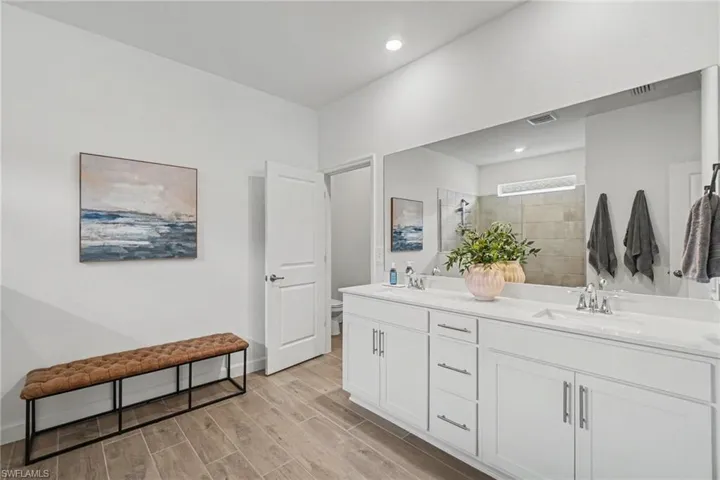 Double vanity featuring white cabinetry, dual integrated sinks, chrome fixtures, and a large-format vanity mirror with wood-finish tile flooring