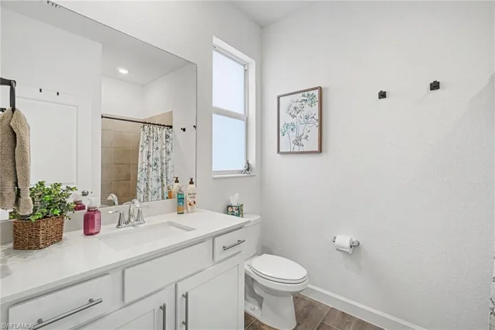 Bathroom featuring a white vanity cabinet, solid-surface countertop with an integrated sink, expansive wall-mounted mirror, polished chrome hardware, and wood-finish tile flooring