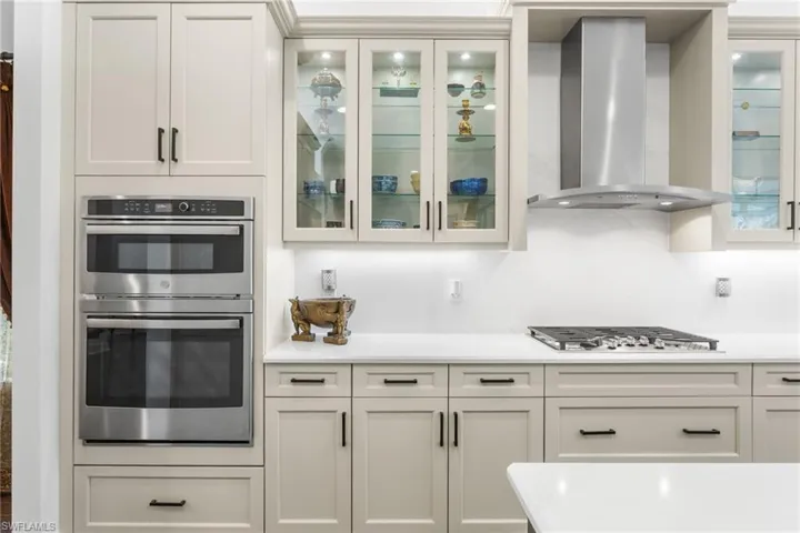 Kitchen with exhaust hood, stainless steel appliances, white cabinets, and light stone counters