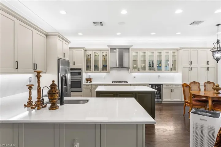 Kitchen with glass insert cabinets, a peninsula, dark wood-type flooring, beverage cooler, and light stone counters