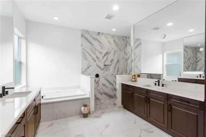 Bathroom featuring two vanities, a marble finish shower, recessed lighting, a bath, and light marble finish flooring