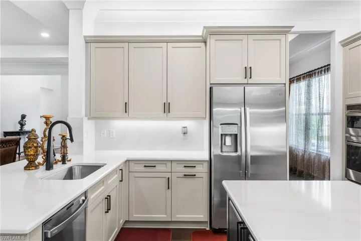Kitchen with light stone counters, stainless steel appliances, a peninsula, recessed lighting, and two tone cabinetry