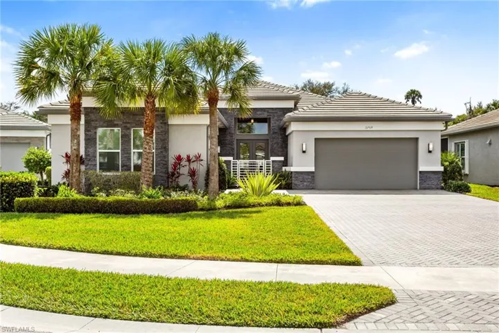 View of front of house featuring stone siding, decorative driveway, an attached garage, stucco siding, and a front yard
