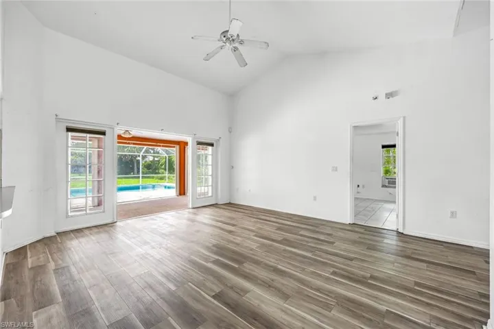 Unfurnished room featuring high vaulted ceiling, healthy amount of natural light, a ceiling fan, and wood finished floors