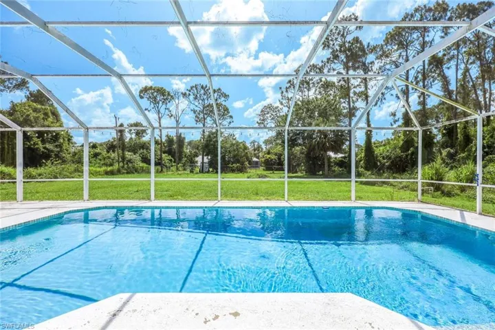 Outdoor pool with view of wooded area, glass enclosure, and a lawn