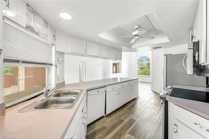 Kitchen featuring appliances with stainless steel finishes, a tray ceiling, a ceiling fan, white cabinets, and wood finished floors