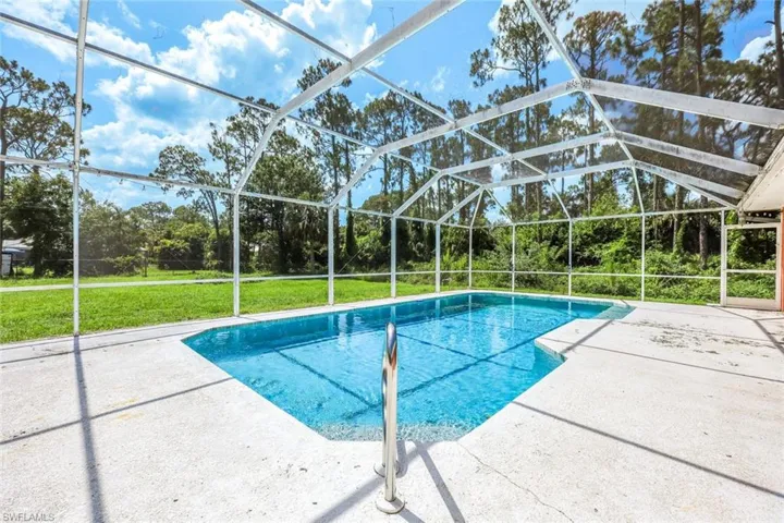 Swimming pool with a patio, a yard, glass enclosure, and view of wooded area