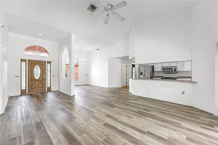 Unfurnished living room with high vaulted ceiling, ceiling fan, arched walkways, wood finished floors, and recessed lighting