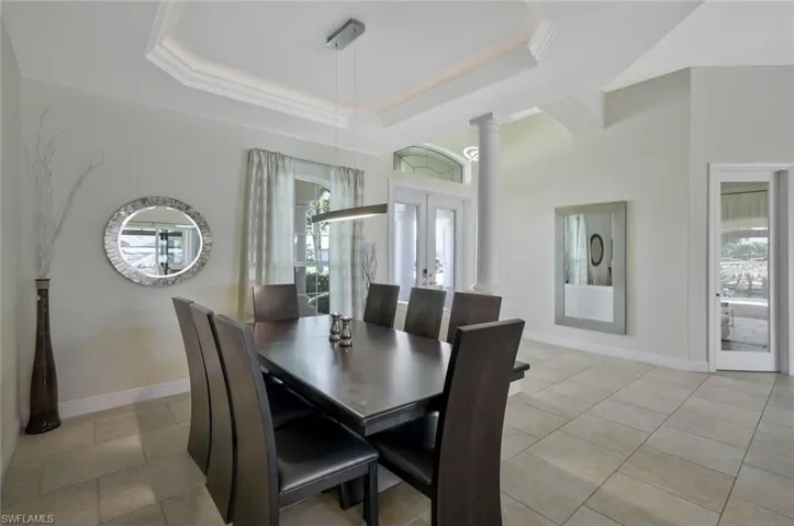 Dining space with french doors, a tray ceiling, decorative columns, and light tile patterned floors