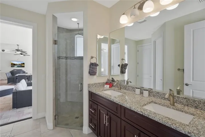 Ensuite bathroom with a shower stall, double vanity, light tile patterned flooring, and a ceiling fan