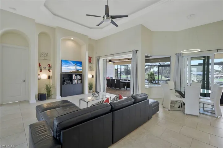 Living area with a tray ceiling, ceiling fan, built in features, light tile patterned floors, and a high ceiling