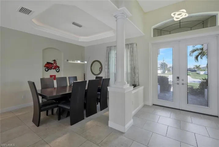 Dining room featuring a raised ceiling, french doors, light tile patterned floors, and ornate columns