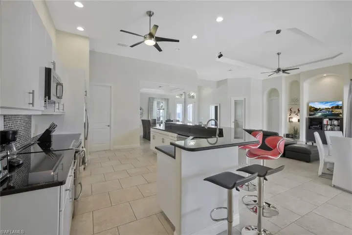 Kitchen featuring a raised ceiling, white cabinetry, ceiling fan, a kitchen bar, and a spacious island