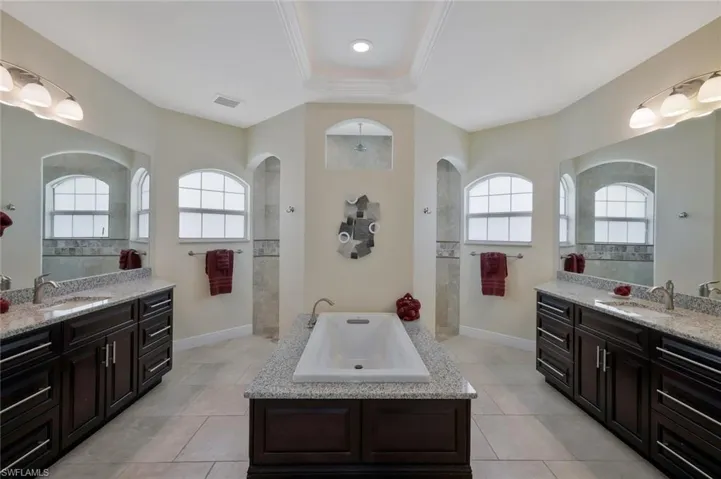 Full bath with two vanities, a bath, walk in shower, and light tile patterned floors