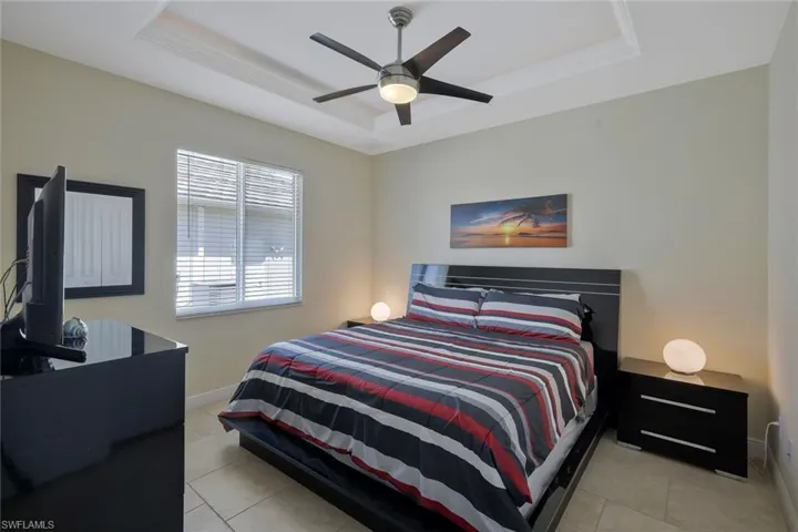Bedroom with a tray ceiling, light tile patterned floors, and a ceiling fan