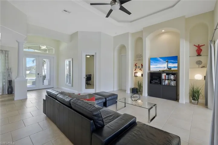 Living room with french doors, light tile patterned floors, a raised ceiling, a ceiling fan, and a towering ceiling