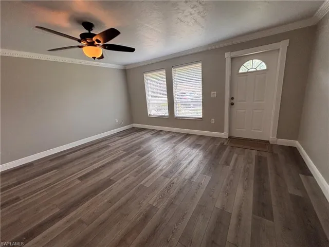 The property features a spacious room with wood-look flooring, neutral wall paint, and crown molding