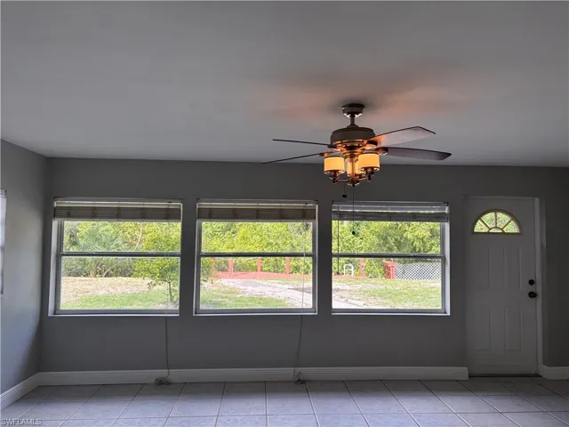 Interior space featuring tiled flooring, a ceiling fan with light fixture, and three windows offering views of lush greenery
