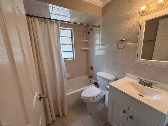 Bathroom featuring a vanity with a white countertop and sink, a mirror with an overhead light fixture, a toilet, a bathtub with a shower, and tiled walls and floor