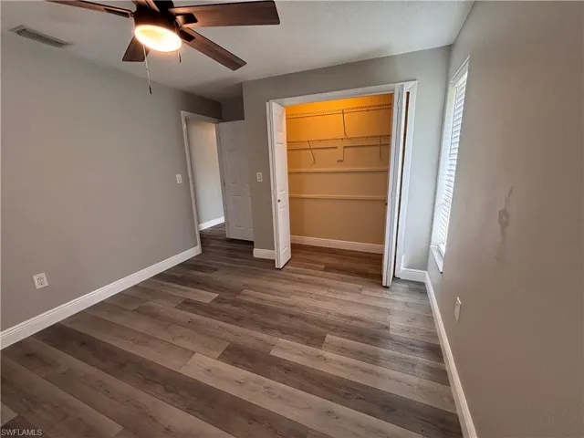 This room features wood-look flooring, light grey walls, and a ceiling fan with an integrated light fixture