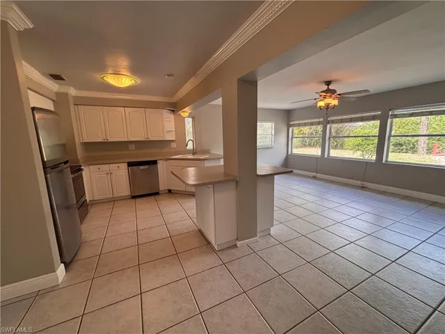Well-appointed kitchen featuring white cabinetry, stainless steel appliances, and a breakfast bar, opening into a spacious living area with tiled floors and large windows