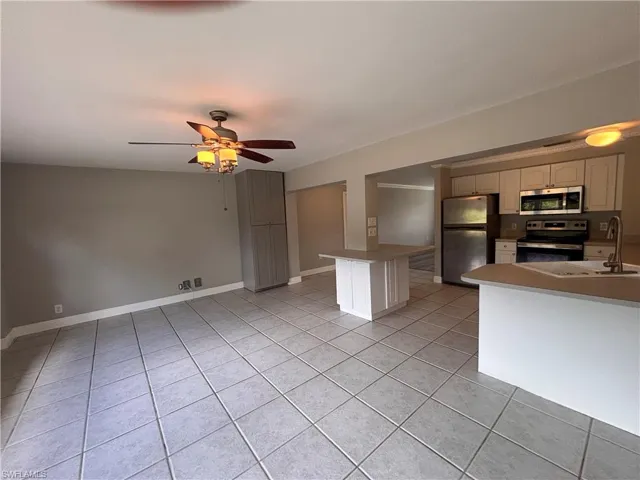 Open concept living area with tiled floors, a ceiling fan, and a kitchen featuring stainless steel appliances and light-colored cabinetry