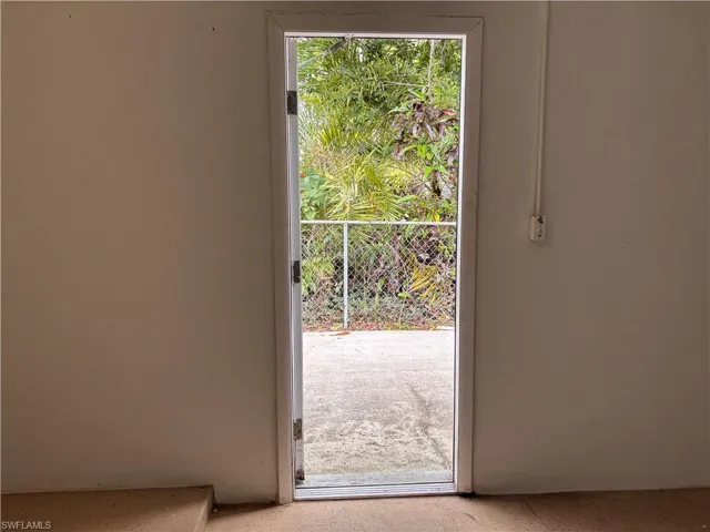 This property includes an exterior door with a screen, opening to a concrete patio area and verdant landscaping