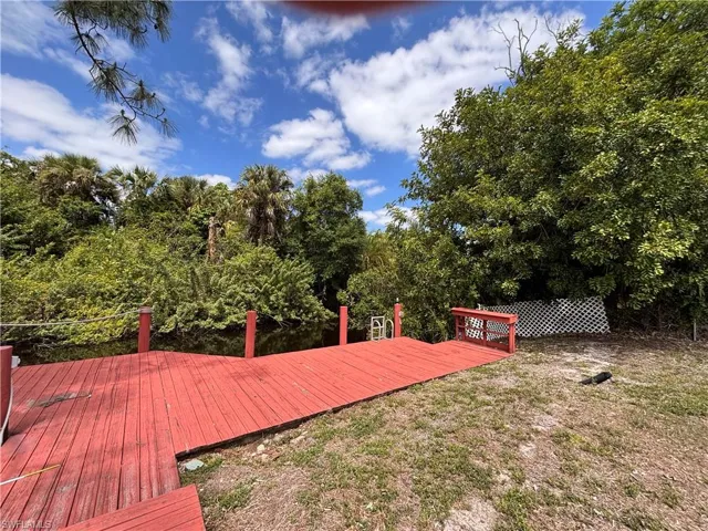 The property features a red wooden deck leading to a waterway, surrounded by lush, mature trees and foliage