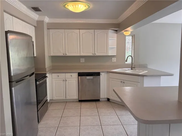 The kitchen features white cabinetry, stainless steel appliances, a double basin sink, crown molding and tile flooring