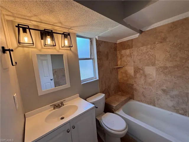 Bathroom featuring a vanity with an integrated sink, a mirror, and a bathtub with tiled surround