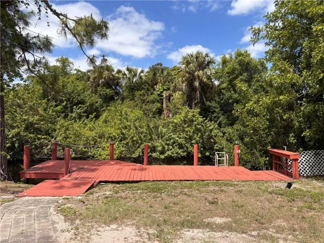 The property features a red wooden deck with posts, a paved pathway, and surrounding foliage