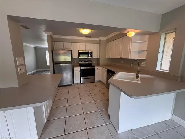 The kitchen features white cabinetry, a double basin sink with a high-arc faucet, and stainless steel appliances