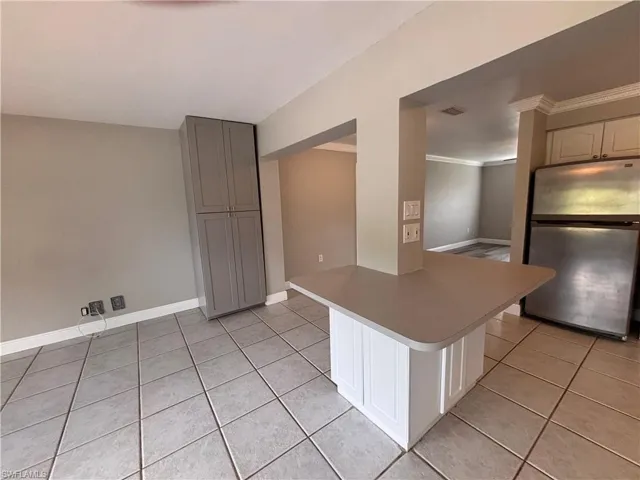 The kitchen features a stainless steel refrigerator, white upper cabinets, and a kitchen island with a light-colored countertop