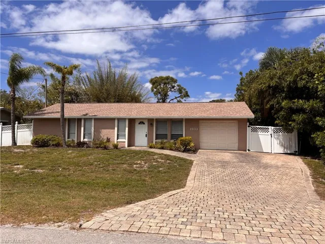 The property features a well-maintained exterior with a paved driveway, a white privacy fence, and mature palm trees