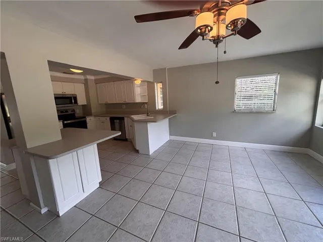 Bright interior space featuring light-colored tile flooring, a ceiling fan with integrated lighting, and a window with blinds