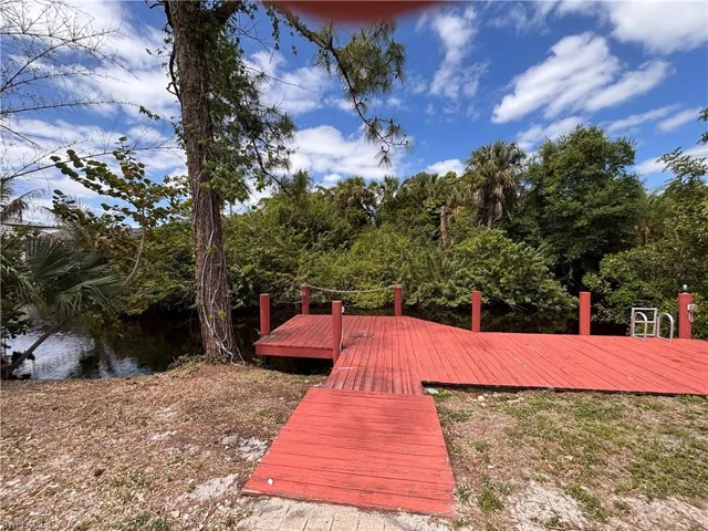 The property features a red dock extending over a body of water, surrounded by lush trees and foliage