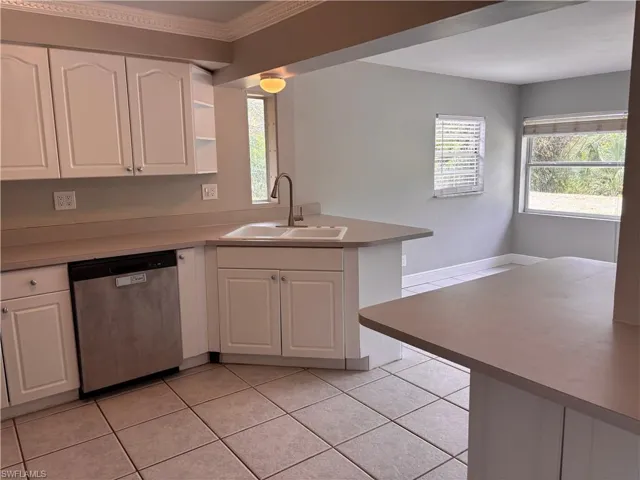 The kitchen features white cabinetry, a double basin sink with a gooseneck faucet, a stainless steel dishwasher, and tile flooring