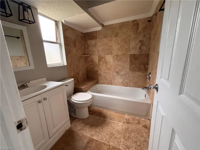 Well-appointed bathroom featuring a bathtub with tiled surround, a window providing natural light, and a vanity with a sink