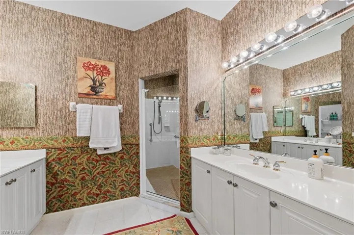 Full bathroom featuring two vanities, wallpapered walls, light tile patterned flooring, and a stall shower