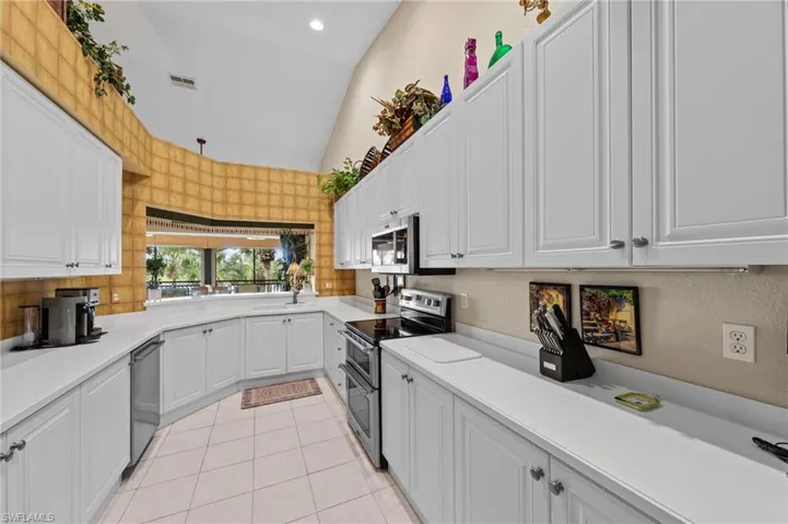 Kitchen featuring white cabinets, stainless steel appliances, lofted ceiling, and recessed lighting