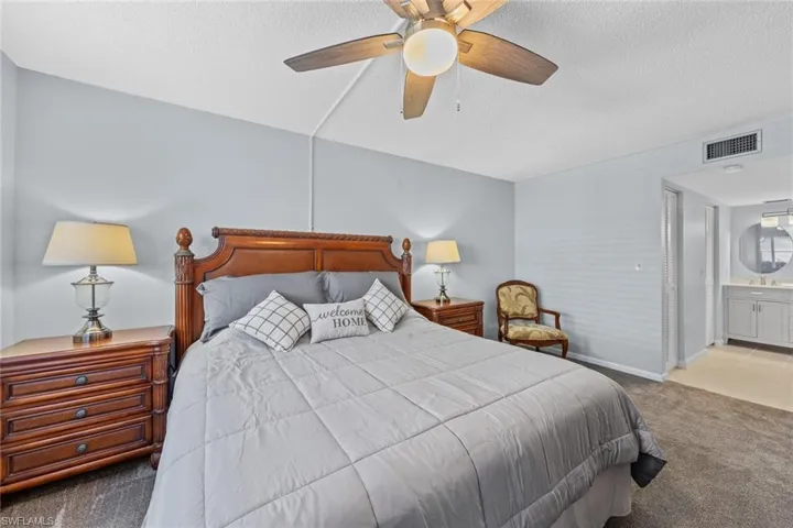 Bedroom with ensuite bathroom, a textured ceiling, light carpet, and ceiling fan