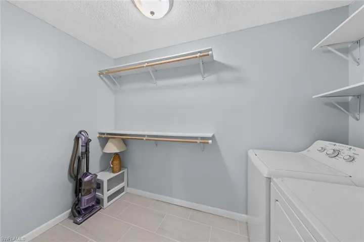 Laundry area featuring light tile patterned floors, a textured ceiling, and washing machine and clothes dryer
