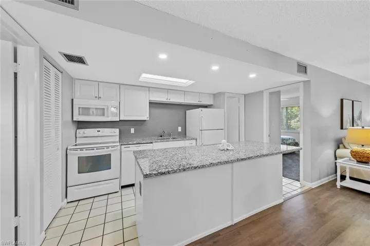 Kitchen with a center island, sink, white cabinets, white appliances, and light hardwood / wood-style flooring
