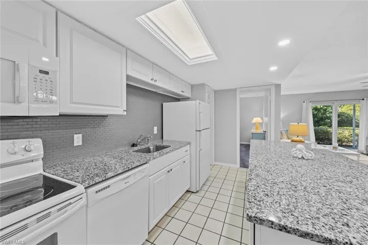 Kitchen featuring tasteful backsplash, light tile patterned flooring, sink, white cabinets, and white appliances