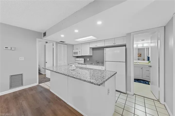 Kitchen with light stone counters, sink, a kitchen island, white cabinetry, and white appliances